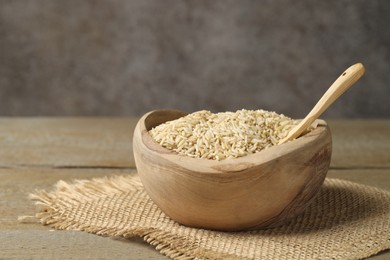 Photo of Raw brown rice in bowl on wooden table against grey background, closeup. Space for text