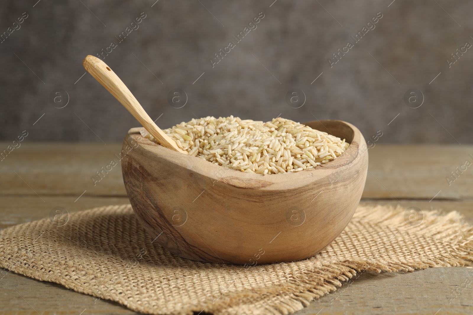 Photo of Raw brown rice in bowl on wooden table against grey background, closeup