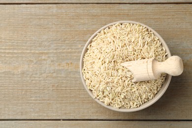 Photo of Raw brown rice and scoop in bowl on wooden table, top view. Space for text