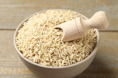 Photo of Raw brown rice and scoop in bowl on wooden table, closeup