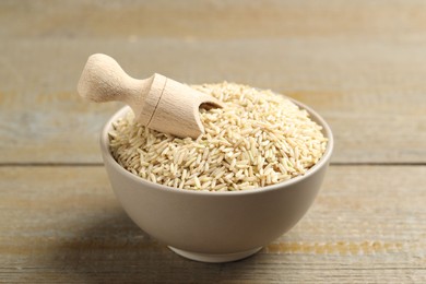 Photo of Raw brown rice and scoop in bowl on wooden table, closeup