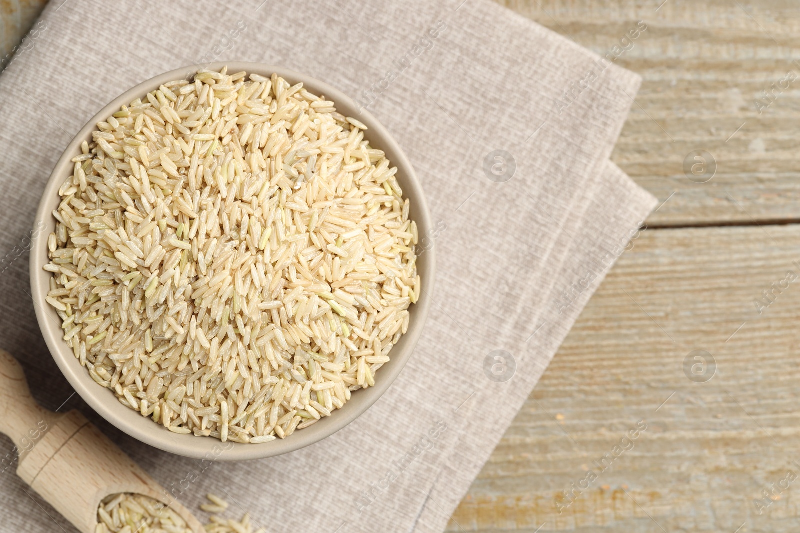 Photo of Raw brown rice in bowl and scoop on wooden table, top view. Space for text