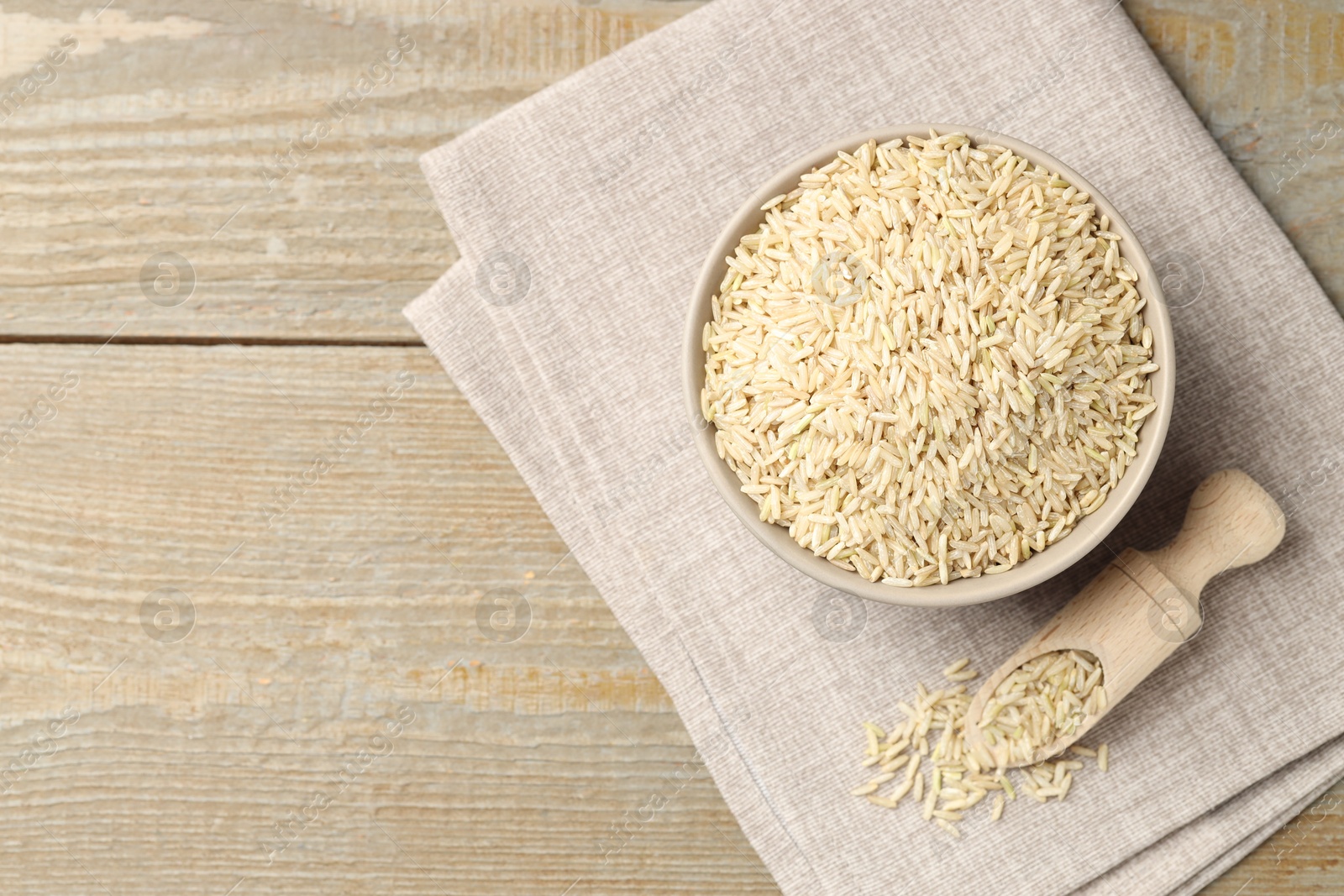 Photo of Raw brown rice in bowl and scoop on wooden table, top view. Space for text