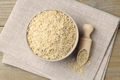 Photo of Raw brown rice in bowl and scoop on wooden table, top view