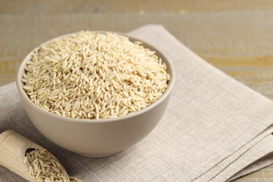 Photo of Raw brown rice in bowl and scoop on table, closeup