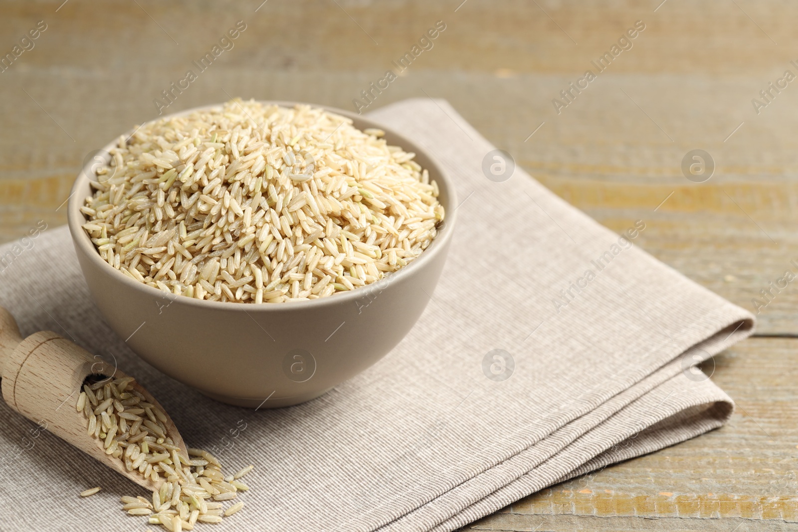 Photo of Raw brown rice in bowl and scoop on wooden table, closeup