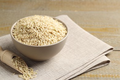 Photo of Raw brown rice in bowl and scoop on wooden table, closeup