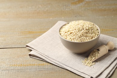 Photo of Raw brown rice in bowl and scoop on wooden table. Space for text