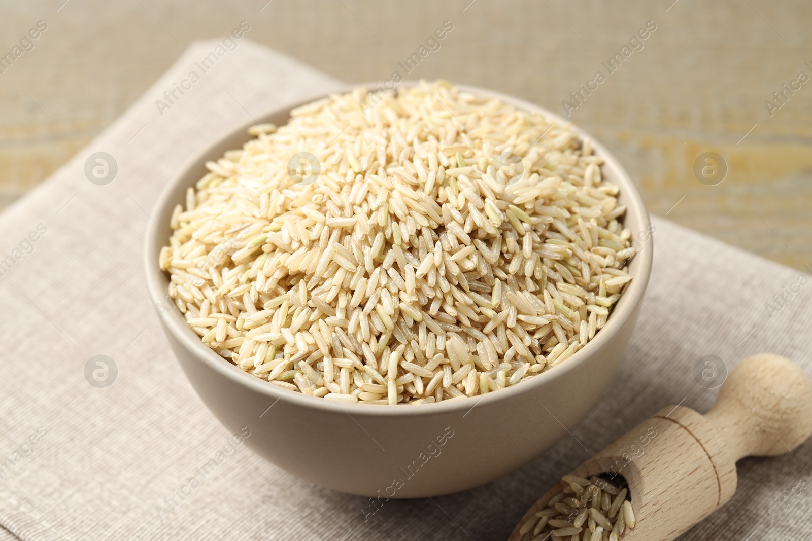 Photo of Raw brown rice in bowl and scoop on table, closeup