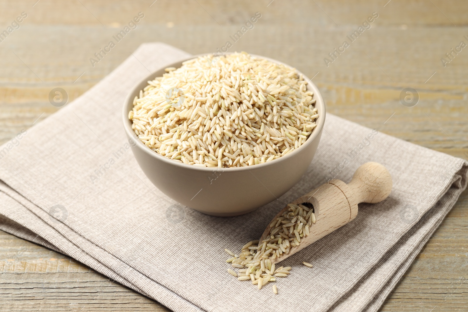 Photo of Raw brown rice and scoop in bowl on wooden table, closeup