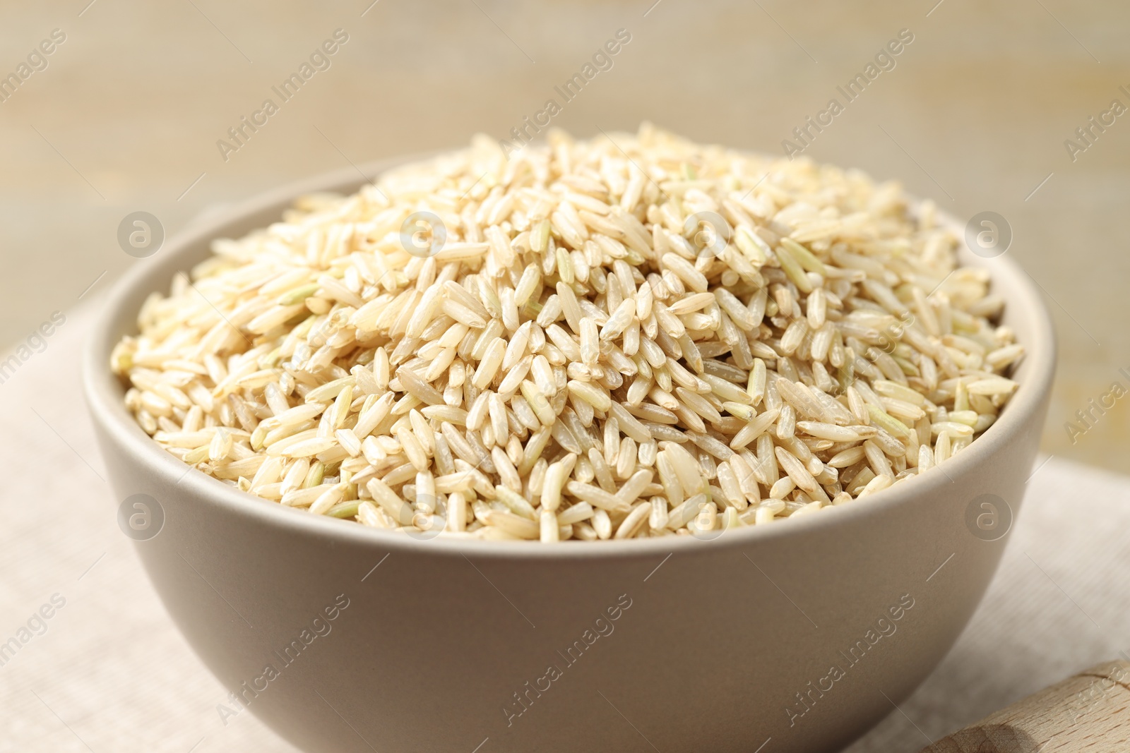 Photo of Raw brown rice in bowl on blurred background, closeup