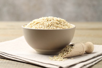 Photo of Raw brown rice in bowl and scoop on wooden table against grey background, closeup