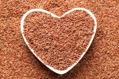 Photo of Pile of brown rice with heart shaped bowl, top view