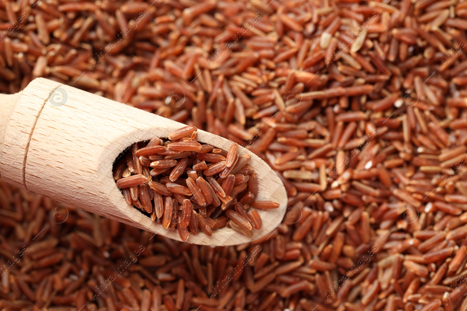 Photo of Brown rice in wooden scoop over pile of grains, top view