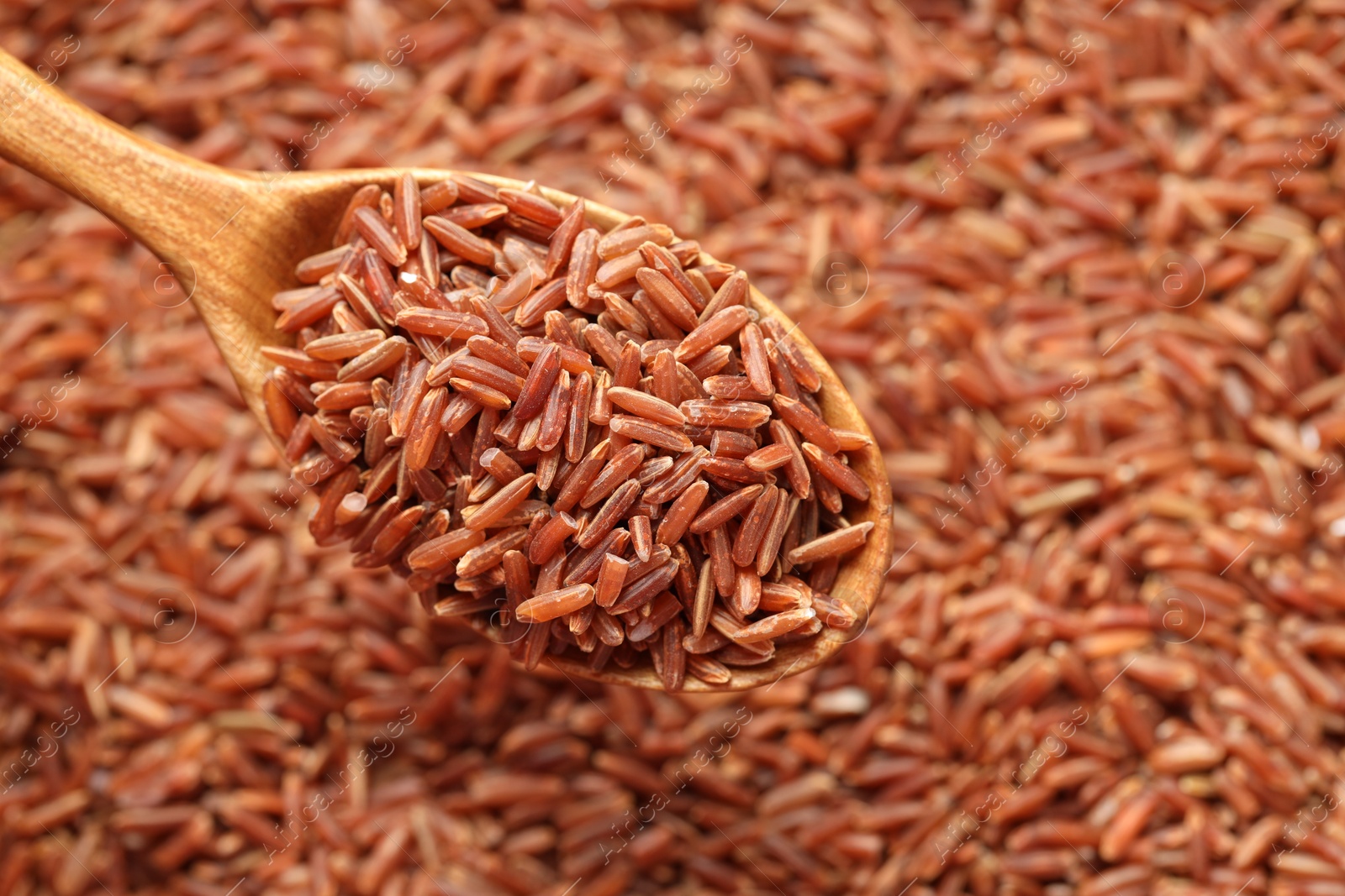 Photo of Pile of brown rice with wooden spoon, top view