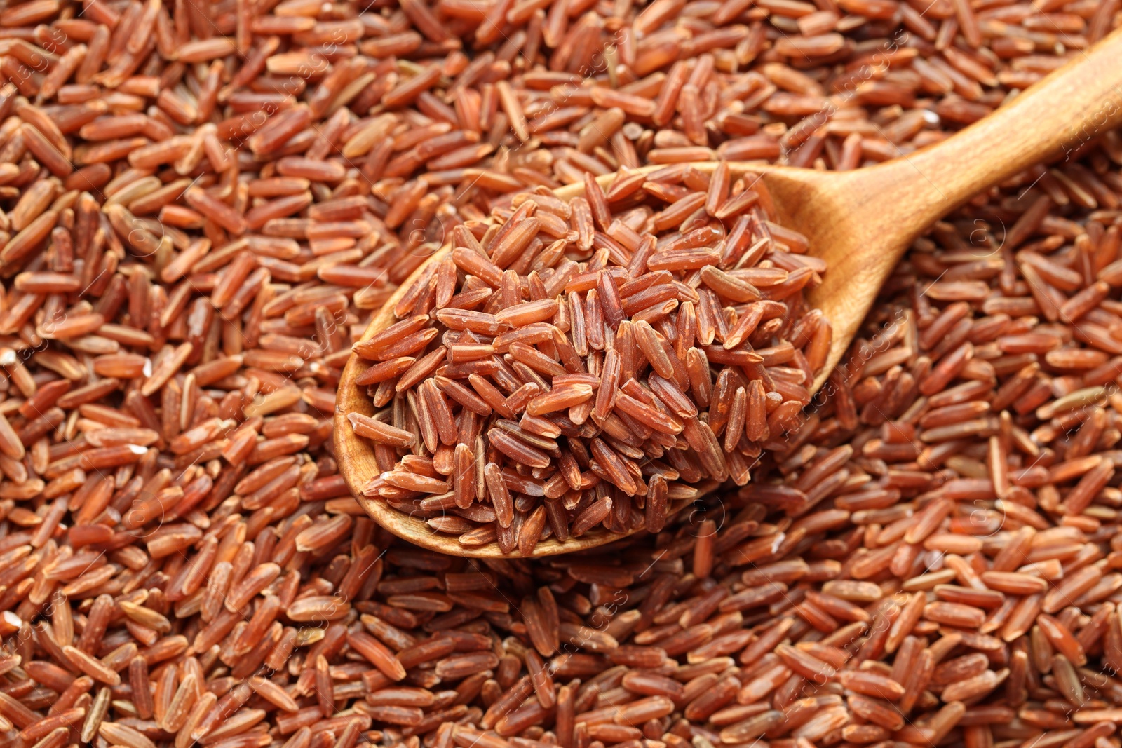 Photo of Pile of brown rice with wooden spoon, top view