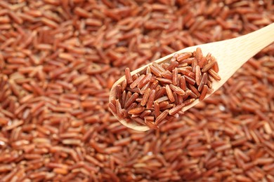 Photo of Brown rice in wooden spoon over pile of grains, closeup. Space for text