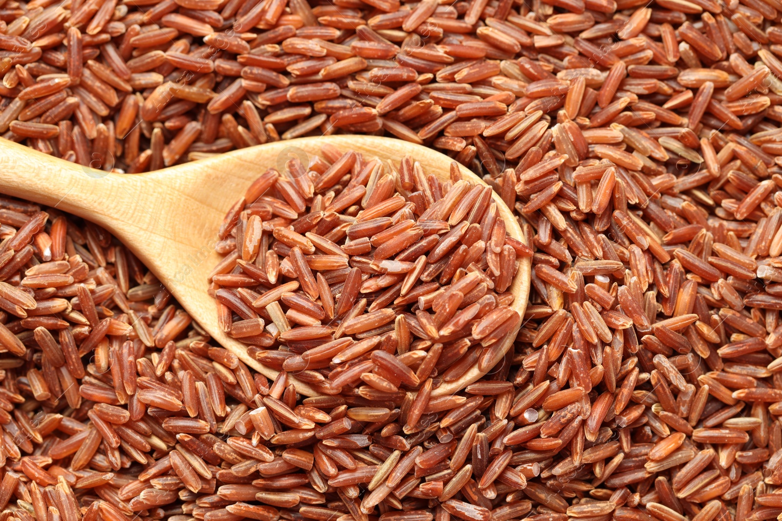 Photo of Pile of brown rice with wooden spoon, top view