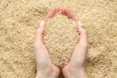 Photo of Woman holding brown rice over pile of grains, top view