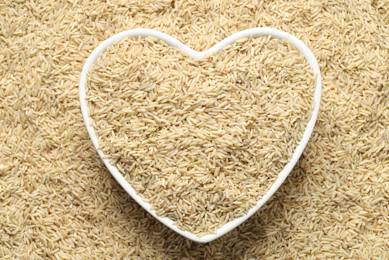 Photo of Pile of brown rice with heart shaped bowl, top view