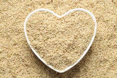 Photo of Pile of brown rice with heart shaped bowl, top view