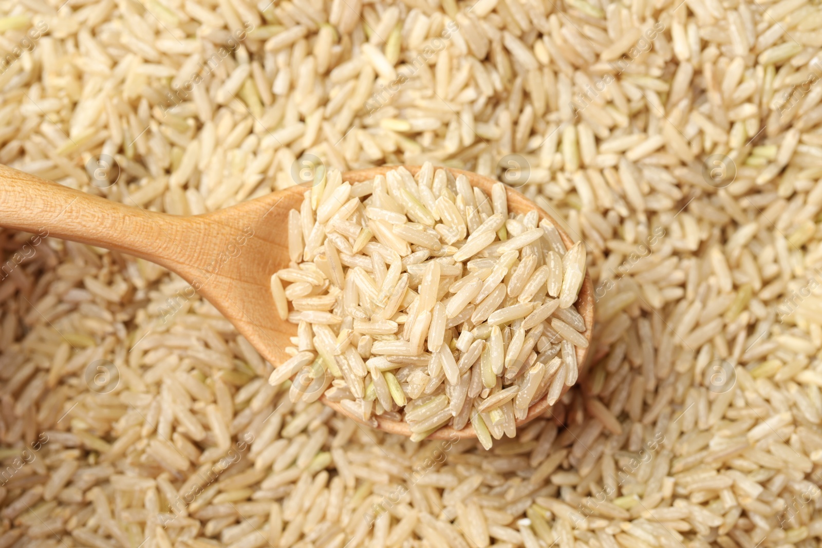 Photo of Pile of brown rice with wooden spoon, top view