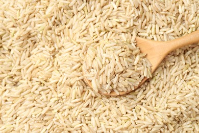 Photo of Pile of brown rice with wooden spoon, top view