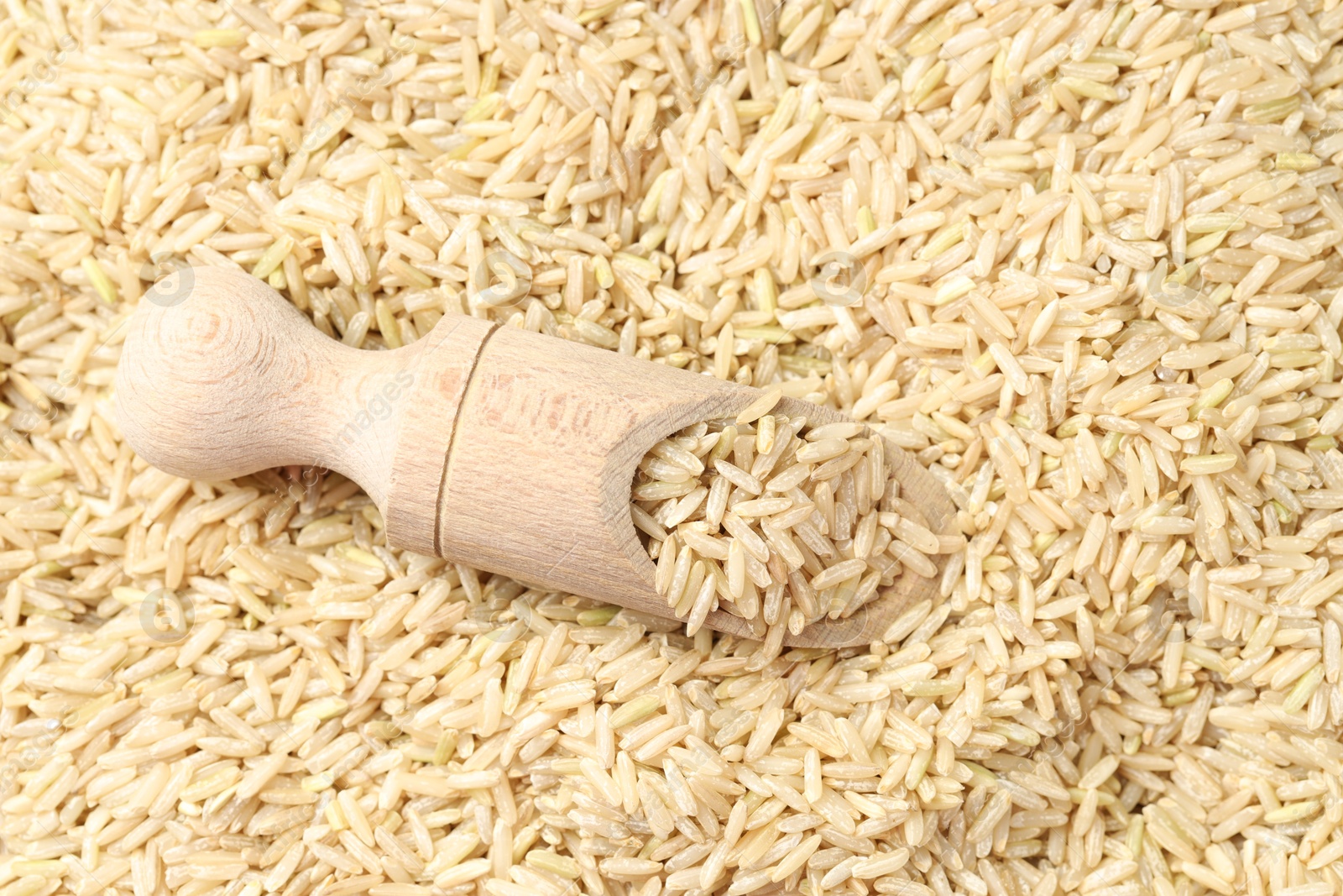 Photo of Pile of brown rice with wooden scoop, top view