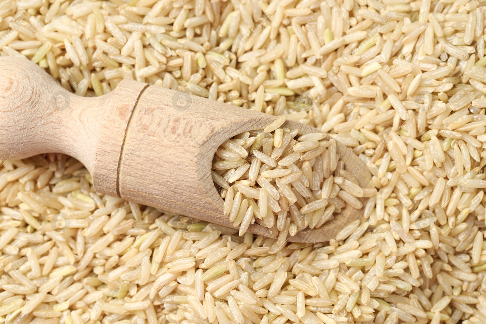 Photo of Pile of brown rice with wooden scoop, top view