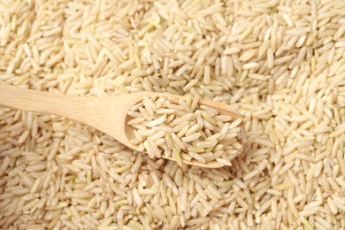 Photo of Brown rice in wooden spoon over pile of grains, top view