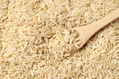 Photo of Pile of brown rice with wooden spoon, top view