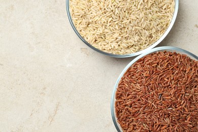 Photo of Different types of brown rice in glass bowls on light grey table, top view. Space for text