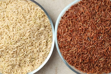 Photo of Different types of brown rice in glass bowls on light grey table, top view