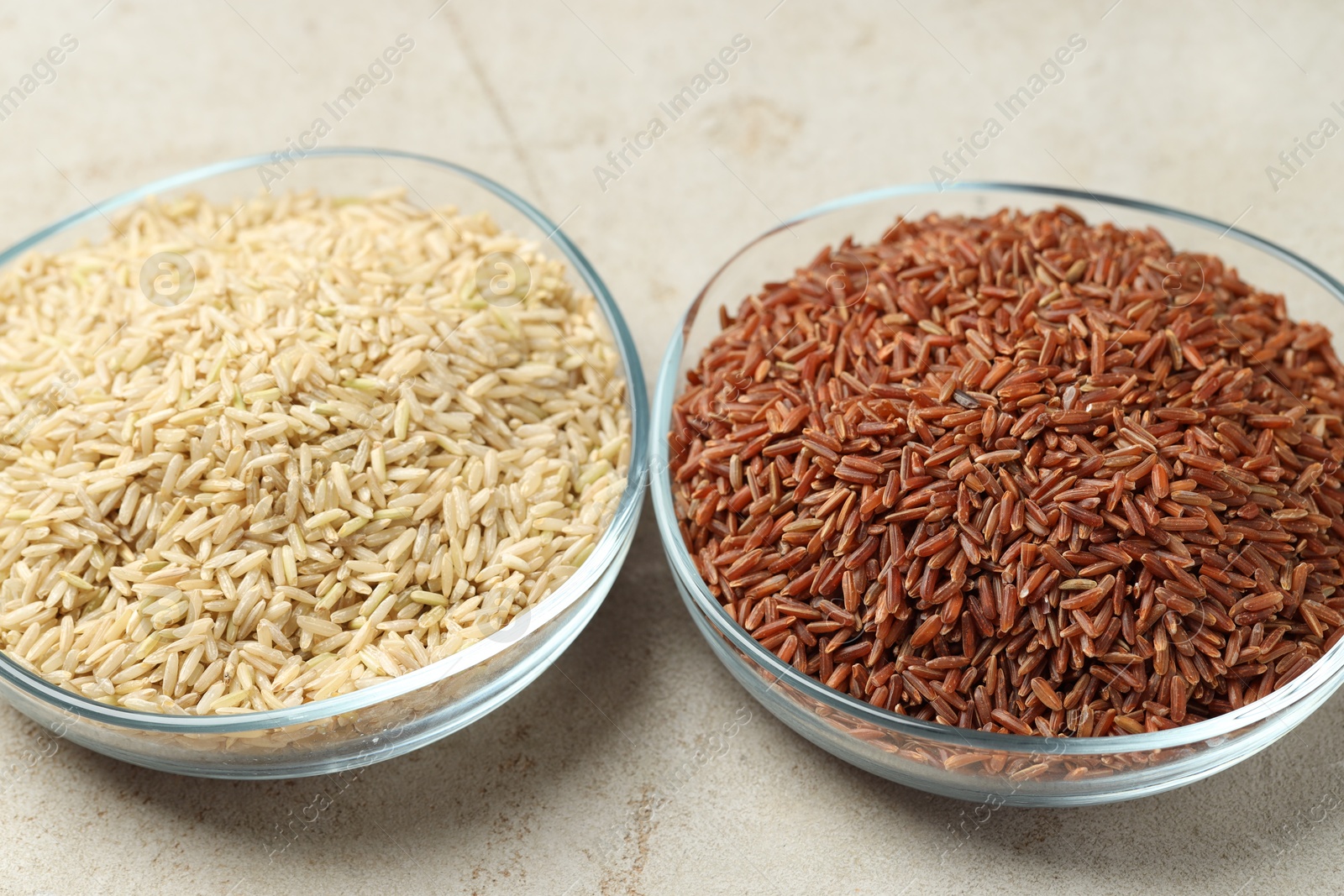 Photo of Different types of brown rice in glass bowls on light grey table, closeup