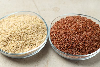 Photo of Different types of brown rice in glass bowls on light grey table, closeup