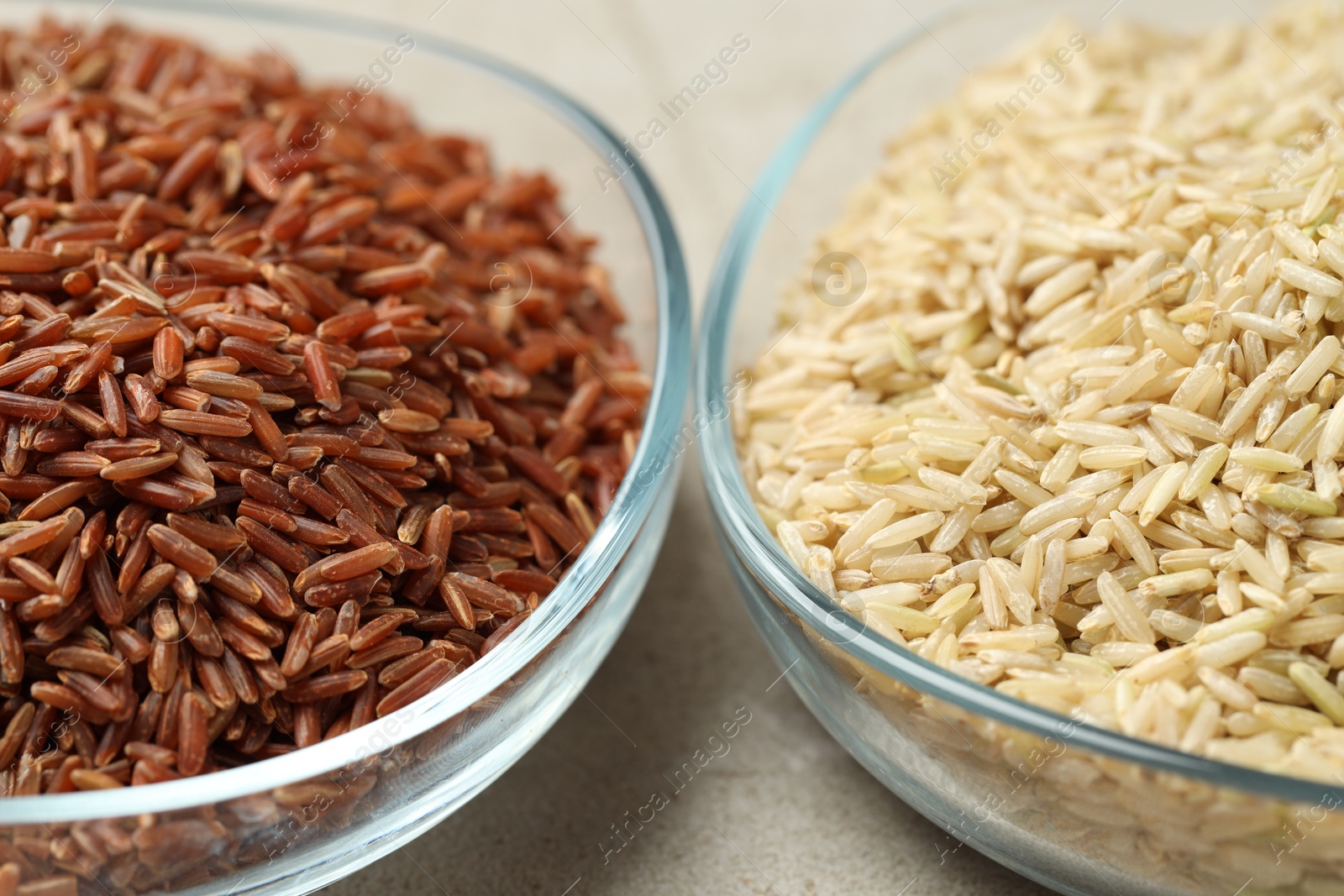 Photo of Different types of brown rice in glass bowls on light grey table, closeup