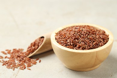 Photo of Brown rice in bowl and scoop on light grey table, closeup