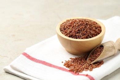 Photo of Brown rice in bowl and scoop on light grey table, closeup. Space for text