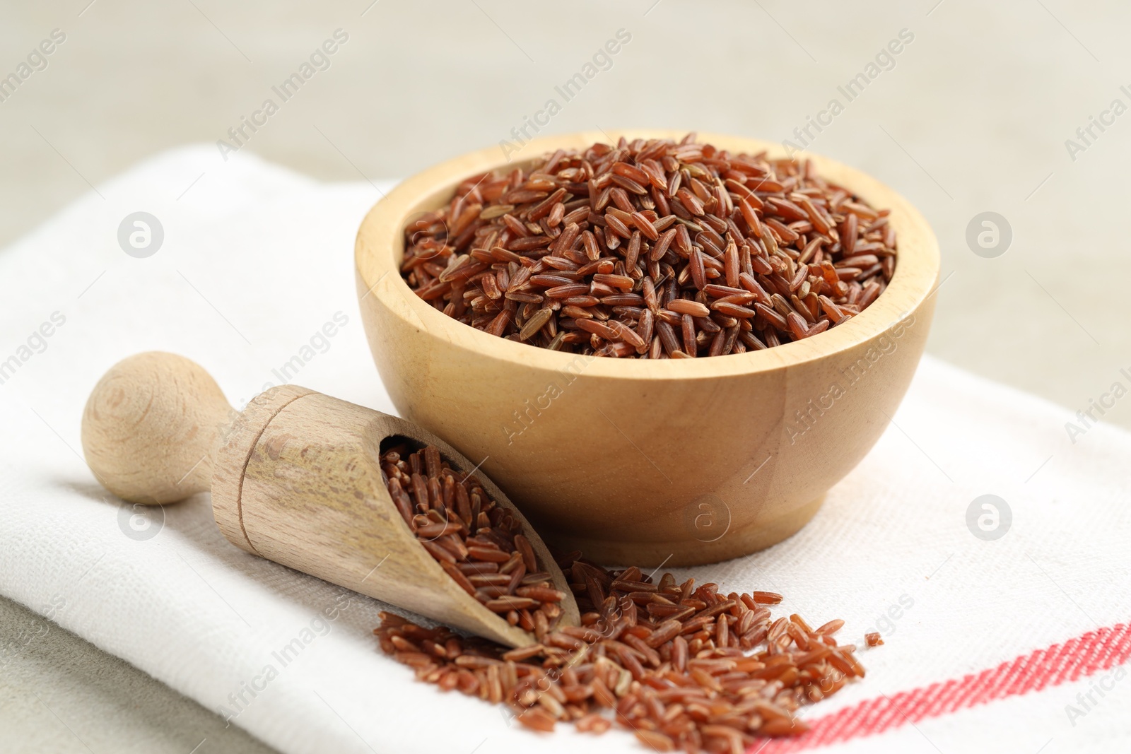 Photo of Brown rice in bowl and scoop on light grey table, closeup