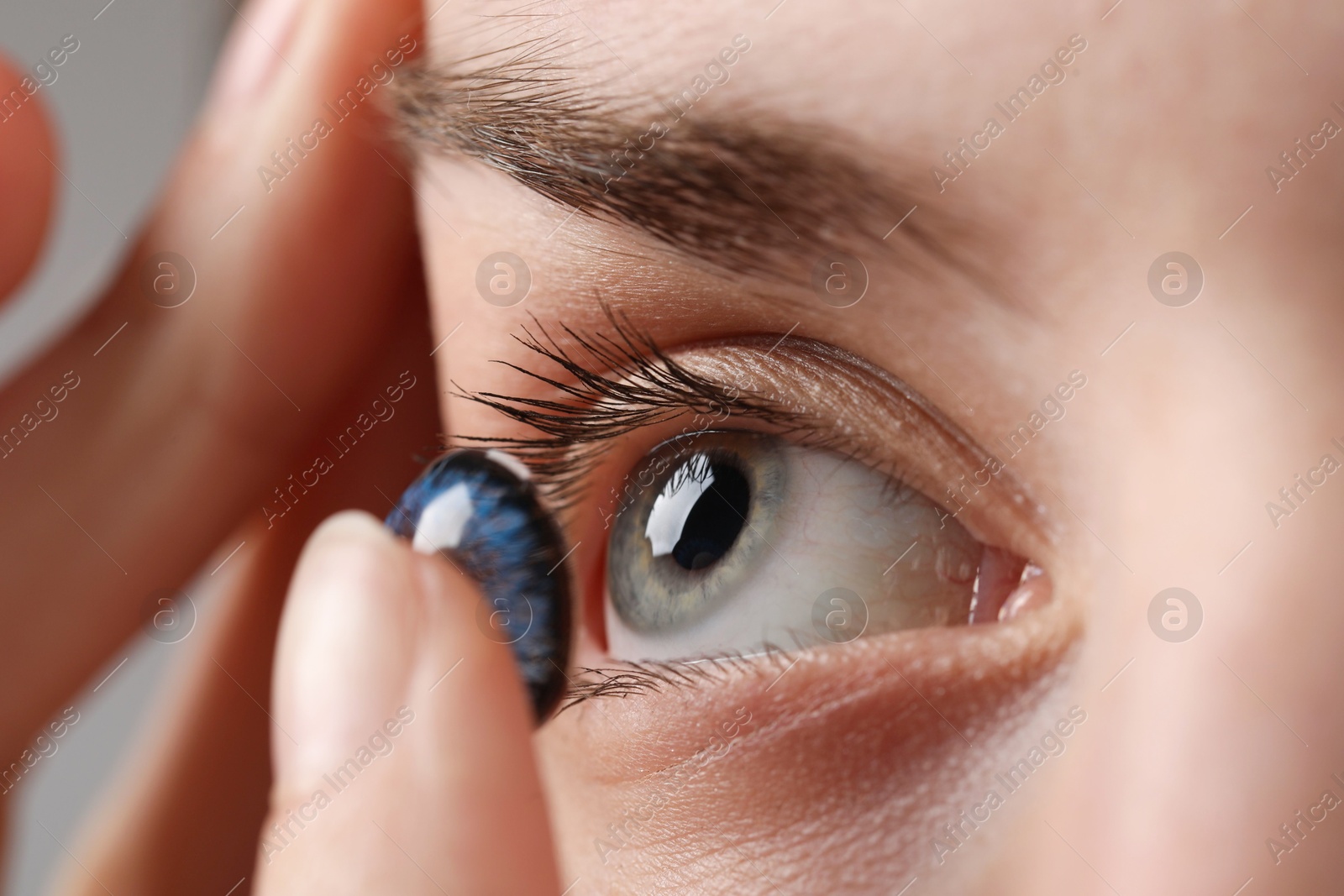 Photo of Woman putting in blue color contact lens, closeup