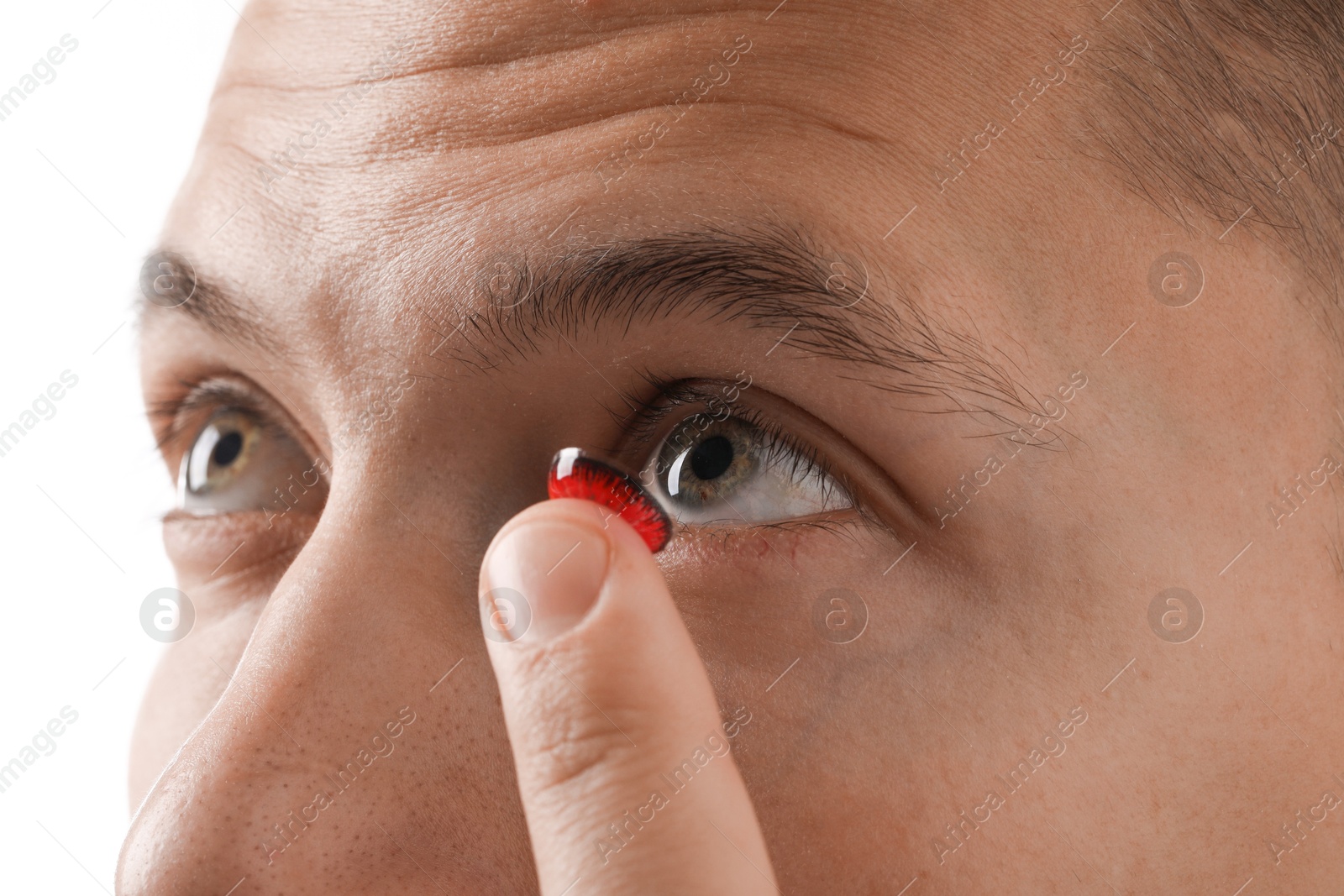 Photo of Man putting color contact lens in his eye on light background, closeup