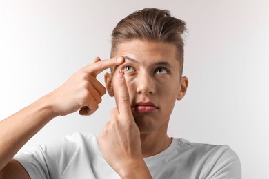 Photo of Man putting color contact lens in his eye on light background