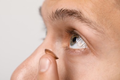 Photo of Man putting color contact lens in his eye on light background, closeup