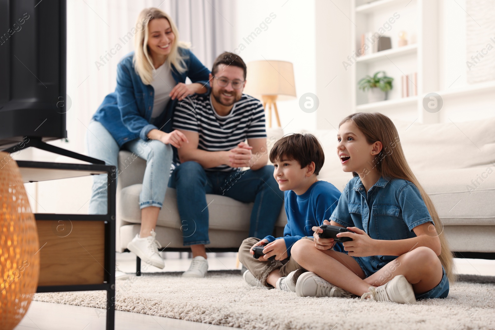 Photo of Cute kids playing video games while their parents resting on sofa at home, selective focus