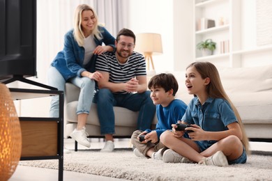 Photo of Cute kids playing video games while their parents resting on sofa at home, selective focus