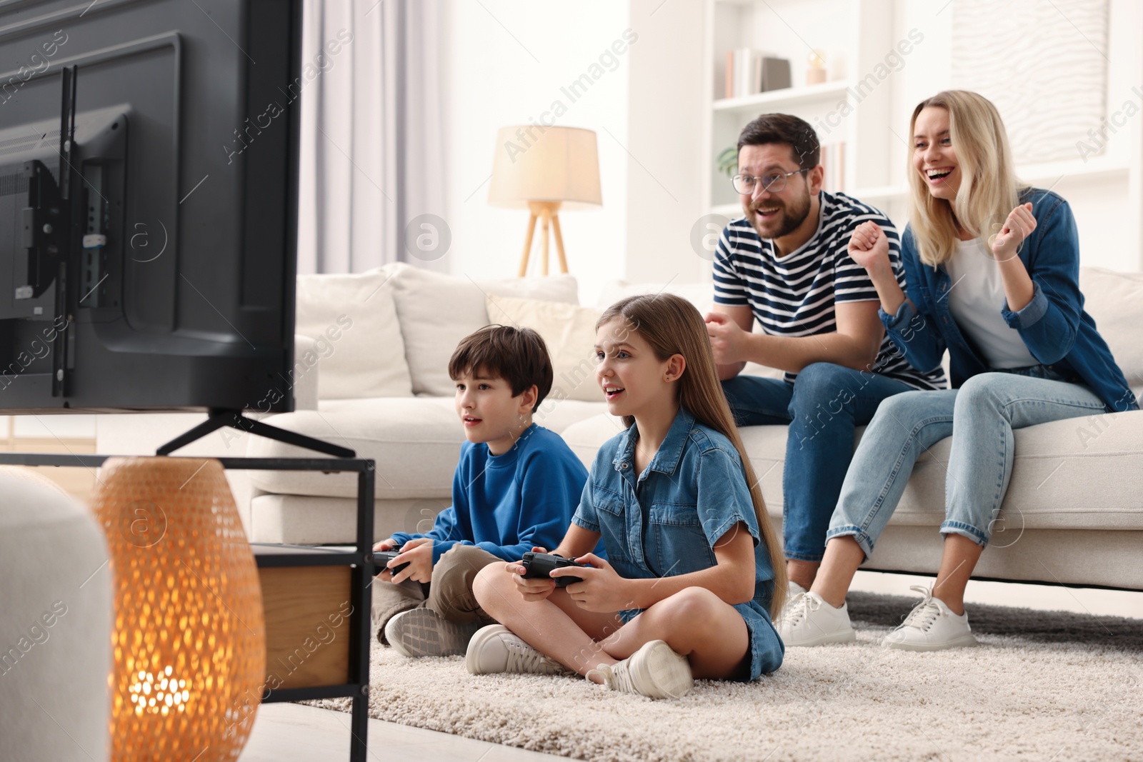 Photo of Cute kids playing video games while their parents resting on sofa indoors