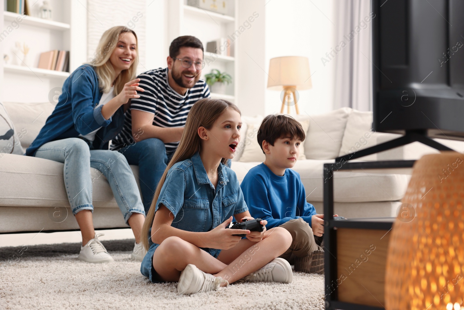 Photo of Cute kids playing video games while their parents resting on sofa at home