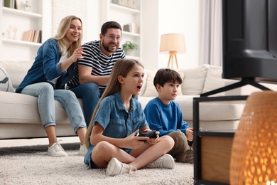 Photo of Cute kids playing video games while their parents resting on sofa at home