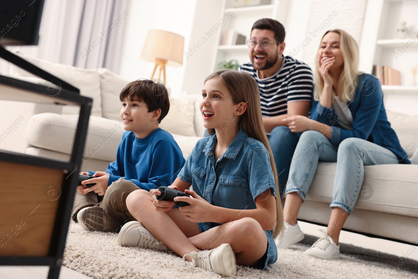 Photo of Cute kids playing video games while their parents resting on sofa at home