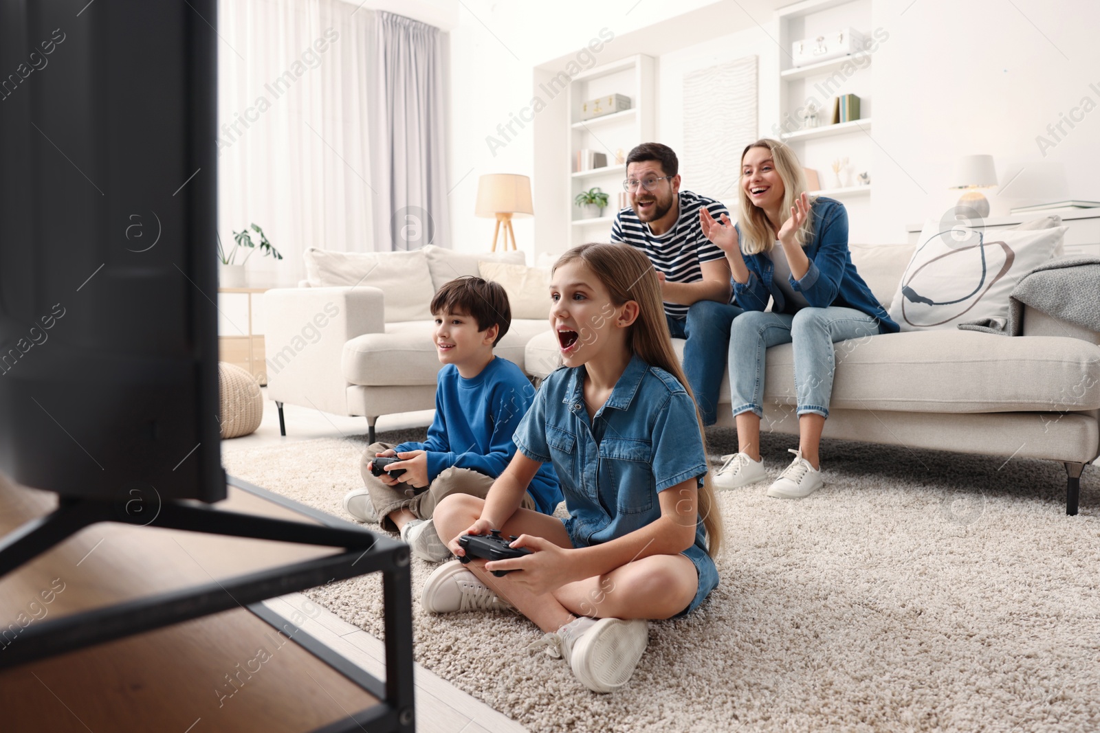 Photo of Cute kids playing video games while their parents resting on sofa indoors